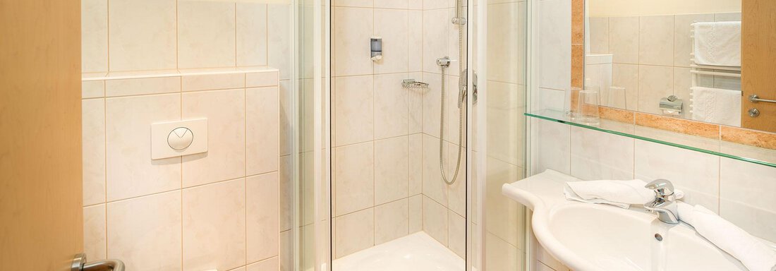 A modern bathroom with a shower cabin and a sink. The walls are tiled in light colors and there is a large mirror. - Gästehaus Europa - Sölden