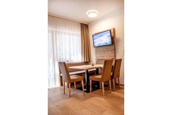 A cozy dining area with a table and four chairs. A large window front ensures plenty of daylight and there is a television on the wall. - Gästehaus Europa - Sölden