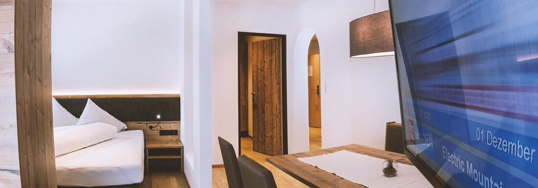 A modern room with a cozy bed and a large television. There is a desk and a chair for work or relaxation. - Gästehaus Europa - Sölden