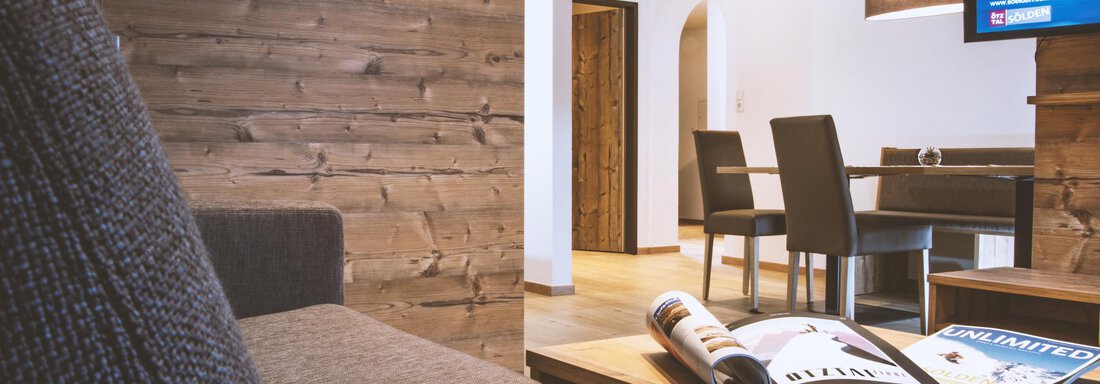 A cozy living room with a modern sofa and a television. In the background, a dining area and wooden paneling are visible. - Gästehaus Europa - Sölden