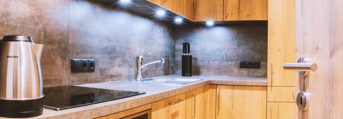 A modern kitchen with wooden cabinets and an elegant design. It features a stainless steel kitchen and good lighting. - Gästehaus Europa - Sölden