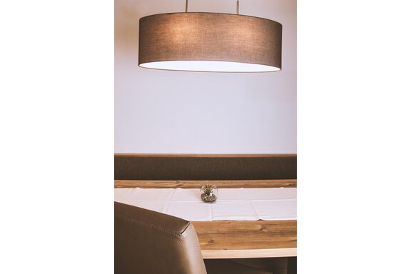 A cozy dining table with a wooden surface and a light table runner. Above the table hangs a stylish lamp. - Gästehaus Europa - Sölden