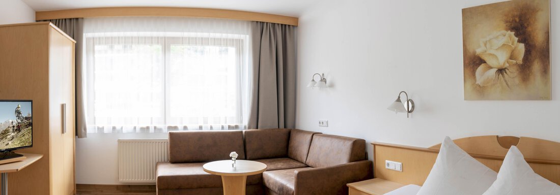 A comfortable hotel room with two beds, a couch, and a table. Large windows provide plenty of daylight. - Gästehaus Europa - Sölden