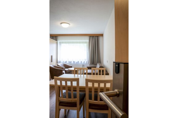 A cozy living room with a large table and chairs. Daylight enters through the window, and there is a comfortable sofa. - Gästehaus Europa - Sölden