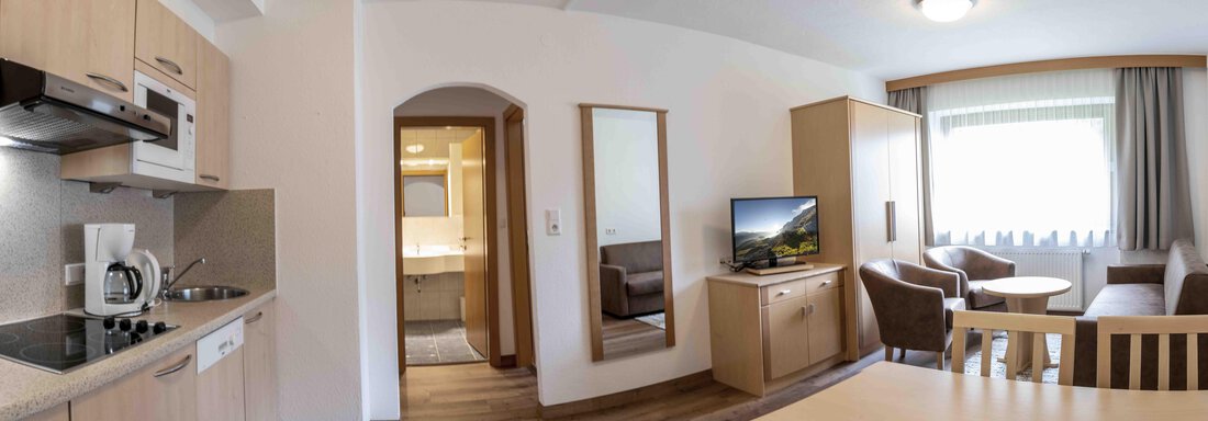 A modern holiday apartment with an open kitchen and a cozy living area. There is a dining area, a TV, and plenty of daylight through the windows. - Gästehaus Europa - Sölden