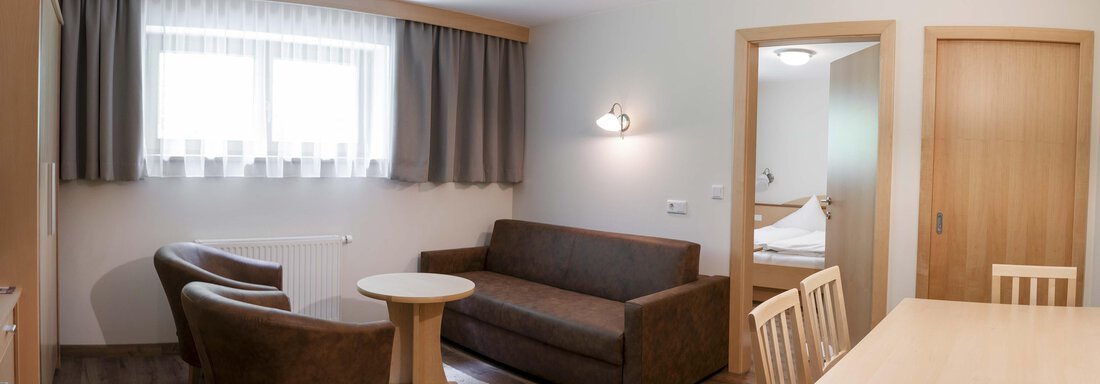 A cozy living area with a sofa, two chairs, and a table. The room has a bright, inviting ambiance with a window that lets in daylight. - Gästehaus Europa - Sölden