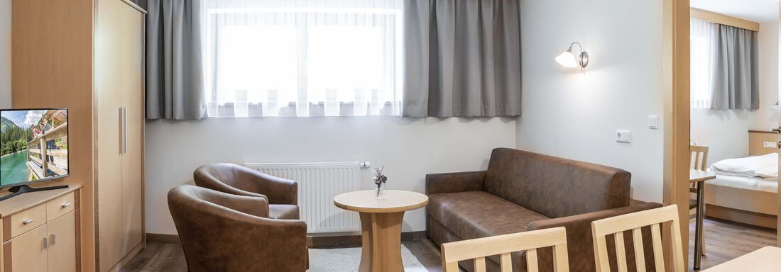 A cozy living space with a sofa, a table, and two chairs. The room has large windows with curtains and gives an inviting impression. - Gästehaus Europa - Sölden