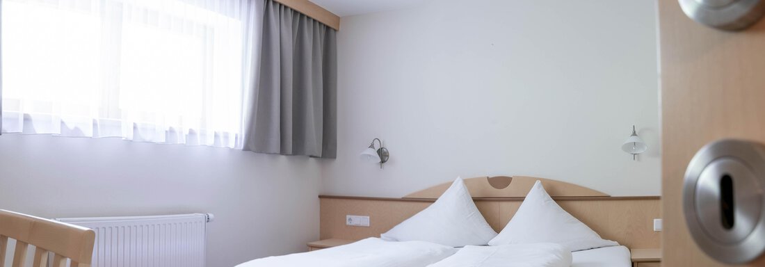A simple bedroom with a double bed and two pillows. The room has a window that provides plenty of daylight. - Gästehaus Europa - Sölden