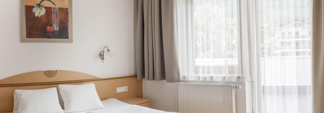 A bright bedroom with two beds and a modern painting on the wall. Large windows let in plenty of daylight and offer a view outside. - Gästehaus Europa - Sölden