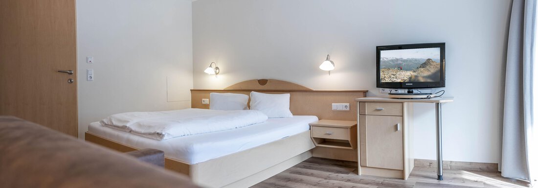 A modern hotel room with a double bed and a television. It has a bright, friendly atmosphere and a simple wooden desk. - Gästehaus Europa - Sölden
