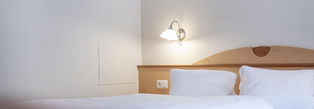 A cozy bedroom with a large bed and soft pillows. A wall lamp provides gentle light. - Gästehaus Europa - Sölden