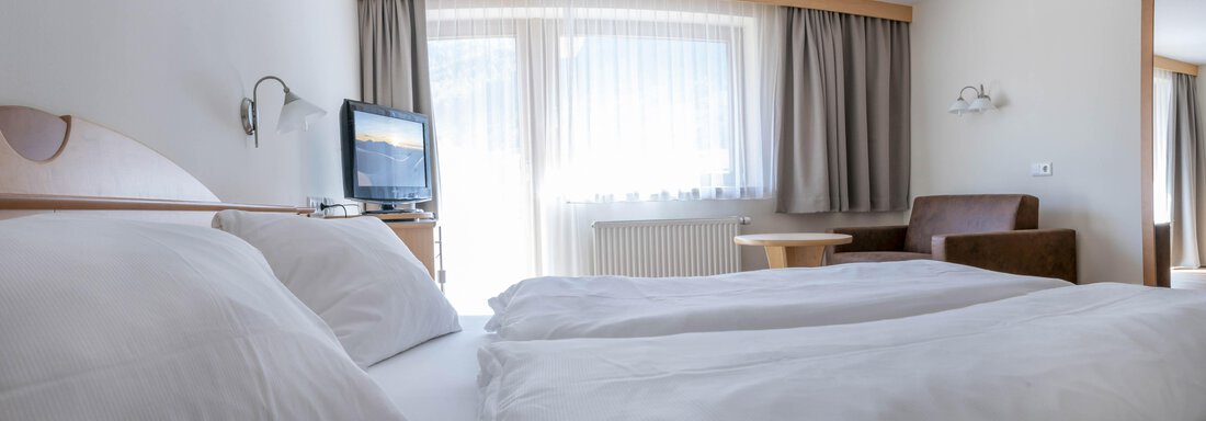 A cozy room with two beds, a TV corner, and large windows. The room design is bright and inviting. - Gästehaus Europa - Sölden