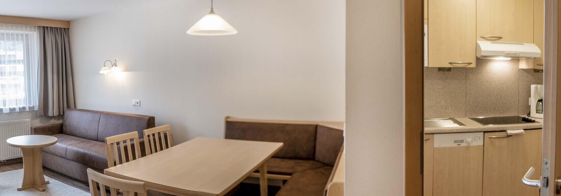 A cozy living area with a dining table and seating. The kitchen is visible in the background and well-equipped. - Gästehaus Europa - Sölden