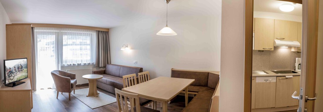 A modern living room with a cozy couch, table, and television. The adjacent kitchen is well-equipped and bright with natural wood tones. - Gästehaus Europa - Sölden