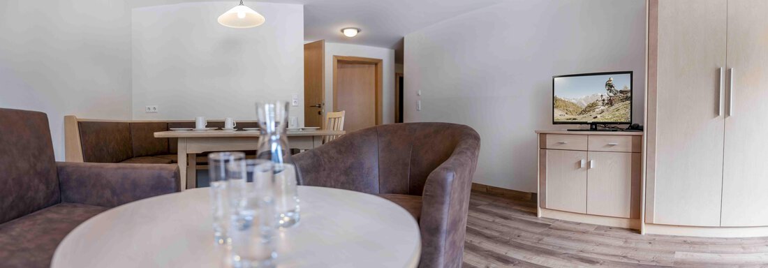 A modern living space with a table, chairs, and two cozy armchairs. A television and a cabinet complement the furnishings. - Gästehaus Europa - Sölden