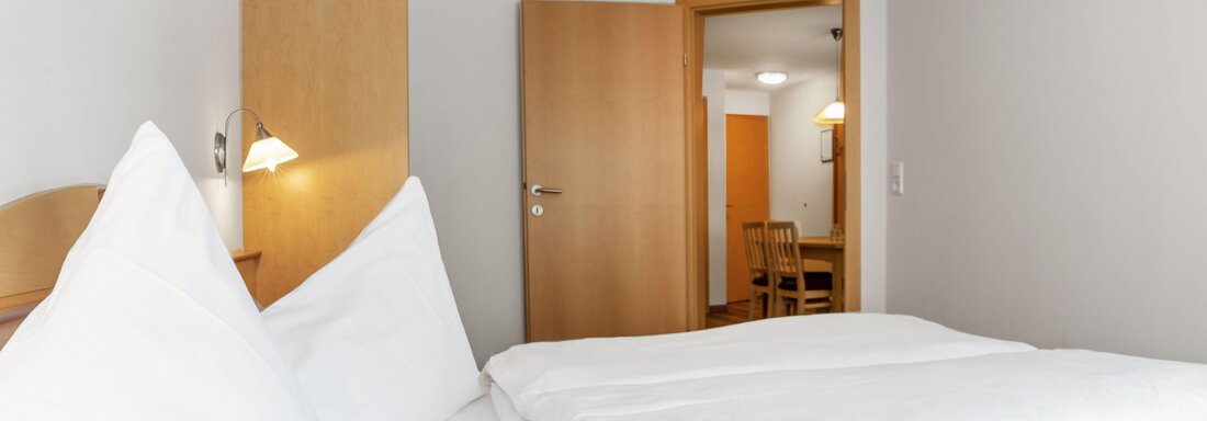 A cozy hotel room with a large bed and bright walls. In the background, there is a door that leads to another room. - Gästehaus Europa - Sölden