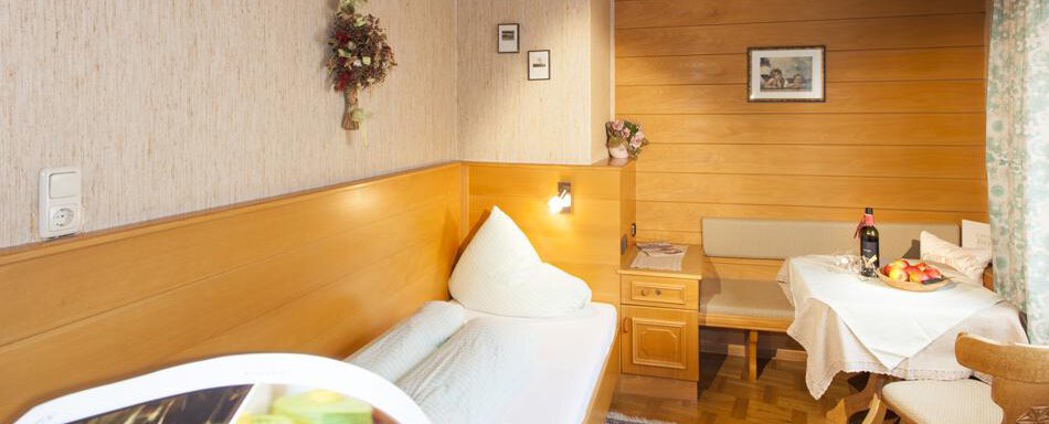 Gaestehaus-Kneisl-Einzelzimmer A cozy room with wood paneling and a single bed. On the table, there is a bottle of wine and fresh fruit. - Gästehaus Kneisl - Sölden