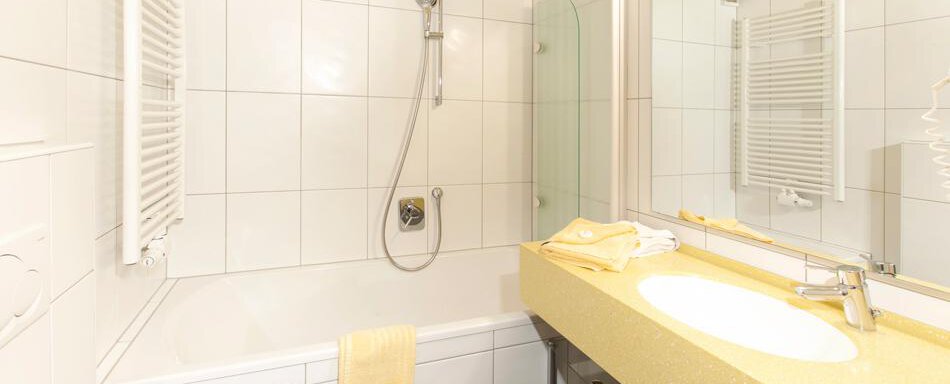 A modern bathroom with a bathtub and a shower. The walls are tiled and there is a sink with a bright workspace. - Gästehaus Kneisl - Sölden