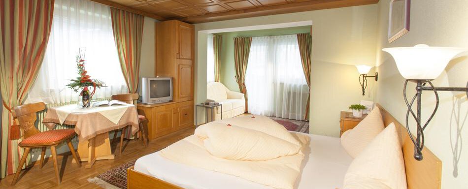 Gaestehaus-Kneisl-Doppelzimmer_Schlafzimmer A cozy room with a double bed, a table, and a television. Large windows let in plenty of daylight. - Gästehaus Kneisl - Sölden