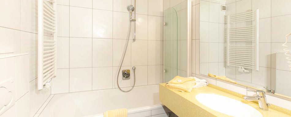 A modern bathroom with a bathtub and a shower. The sink area is bright with yellow accents and a large mirror. - Gästehaus Kneisl - Sölden