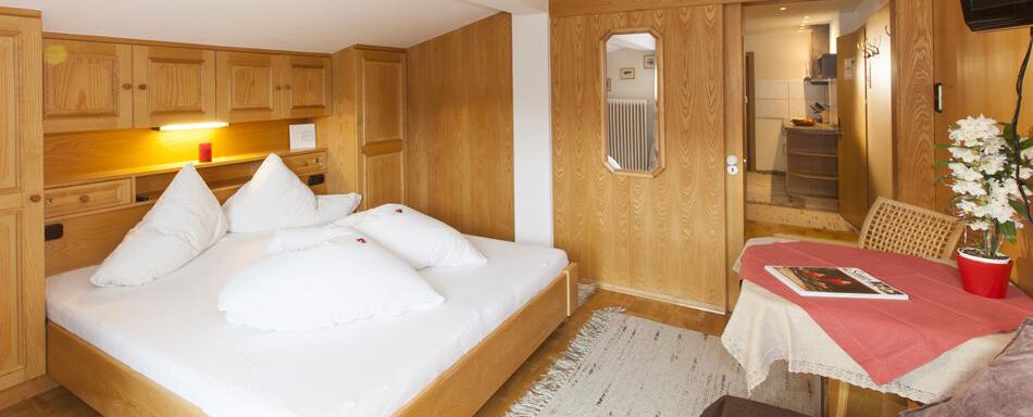 Gaestehaus-Kneisl-Apart-Deluxe1 A cozy room with a double bed and wood paneling. There is a small dining area with a table and chairs, as well as a well-equipped kitchen. - Gästehaus Kneisl - Sölden