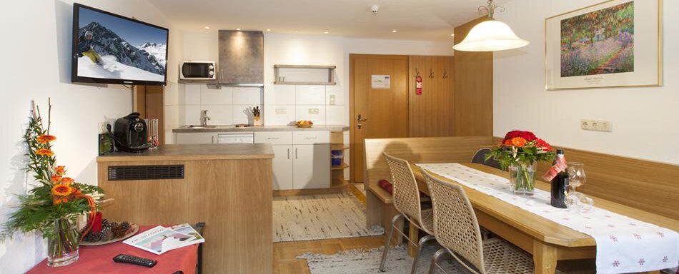 A cozy holiday apartment with a modern kitchen and a dining area. Fresh flowers and some snacks are arranged on the table. - Gästehaus Kneisl - Sölden
