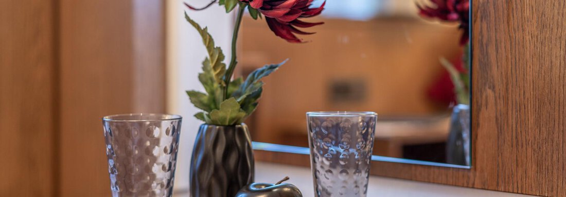 A decorative tray with a floral arrangement and two glasses. In the background, a mirror reflects. - Gästehaus Maier - Sölden