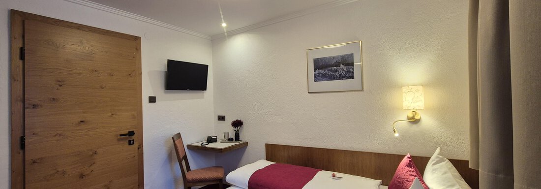 A cozy hotel room with a single bed and a chair. The room is brightly lit and has a television as well as large windows. - Gästehaus Maier - Sölden
