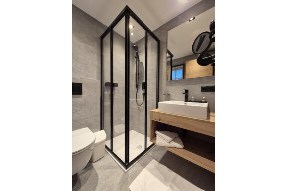 A modern bathroom with a shower. The room has bright tiles and a large mirror. - Gästehaus Maier - Sölden