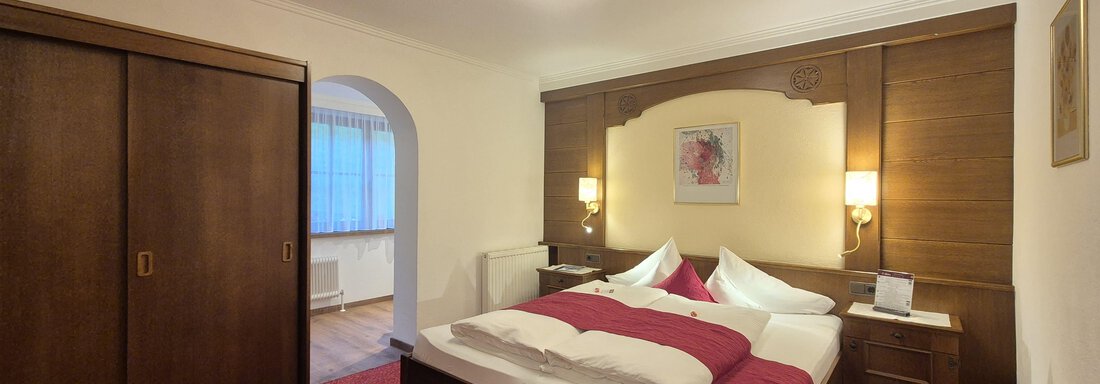 A cozy bedroom with a large double bed and modern television. The room is warmly decorated and has a red carpet. - Gästehaus Maier - Sölden