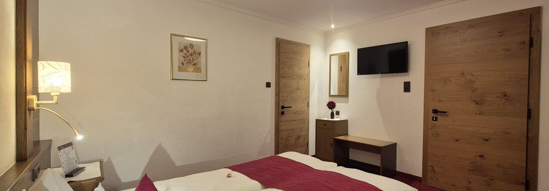A cozy bedroom with a large double bed and modern television. The room is warmly decorated and has a red carpet. - Gästehaus Maier - Sölden