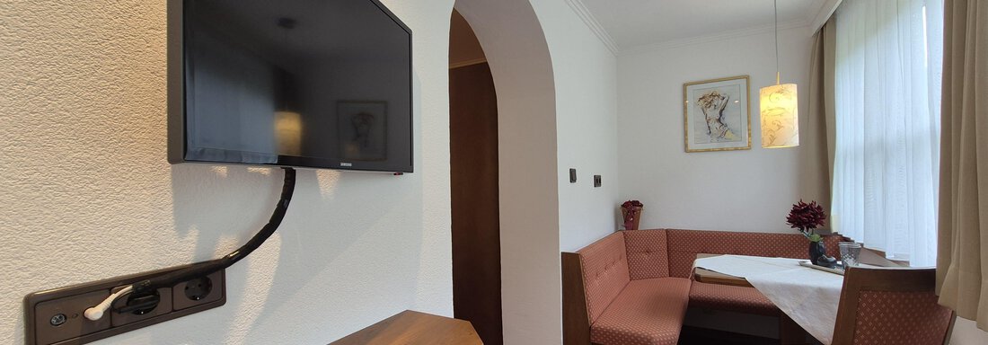 A light-filled room with a sitting area, a TV, and a coat rack. - Gästehaus Maier - Sölden