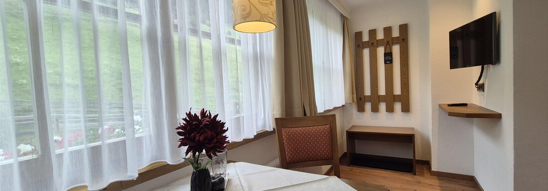 A light-filled room with a sitting area, a TV, and a coat rack. - Gästehaus Maier - Sölden