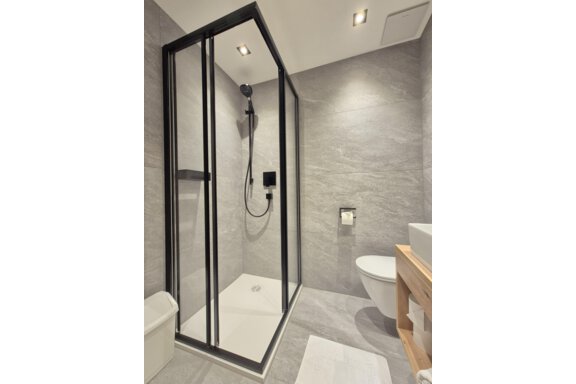 A modern bathroom with a shower. The room has bright tiles and a large mirror. - Gästehaus Maier - Sölden