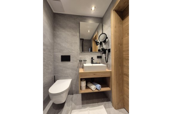 A modern bathroom with a shower. The room has bright tiles and a large mirror. - Gästehaus Maier - Sölden