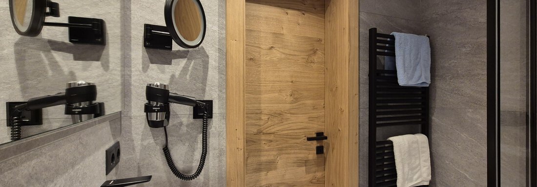 A modern bathroom with a shower. The room has bright tiles and a large mirror. - Gästehaus Maier - Sölden