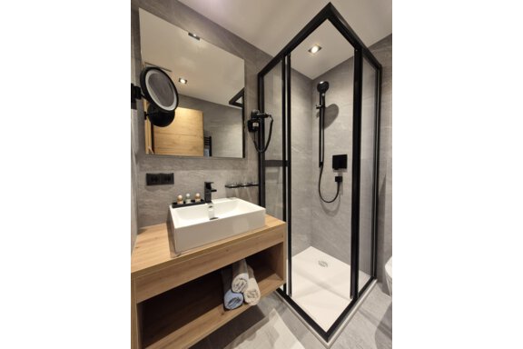 A modern bathroom with a shower. The room has bright tiles and a large mirror. - Gästehaus Maier - Sölden