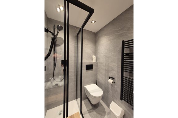 A modern bathroom with a shower. The room has bright tiles and a large mirror. - Gästehaus Maier - Sölden