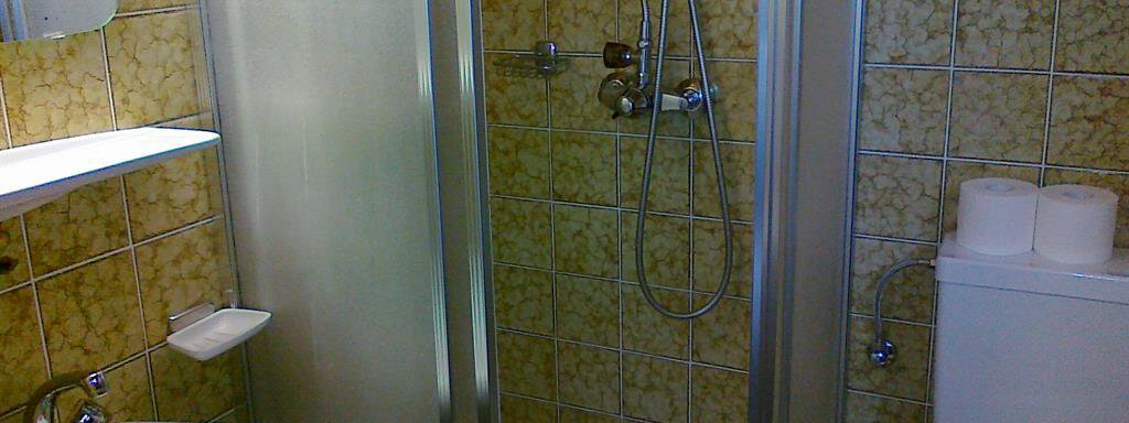A small bathroom with a shower, a sink, and a toilet. The walls are tiled with yellow tiles. - Gästehaus Martin - Sölden