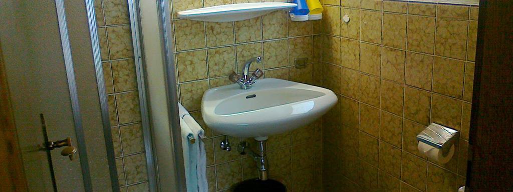 A small bathroom with a shower, a sink, and a toilet. The walls are tiled and there is a window for natural light. - Gästehaus Martin - Sölden