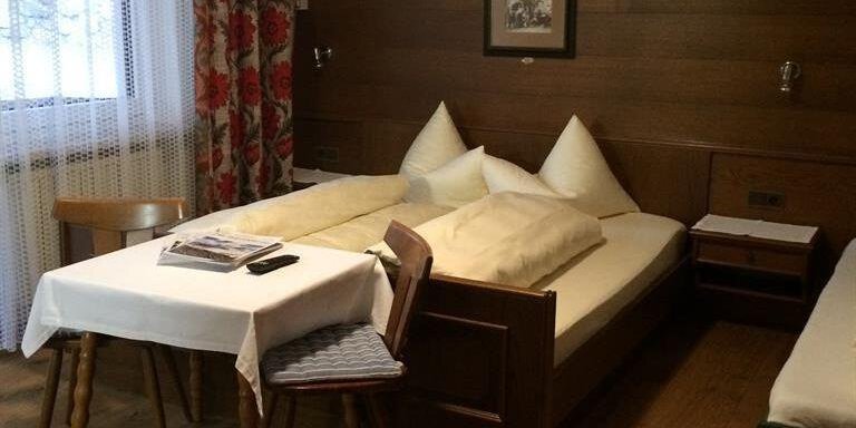 A cozy bedroom with two beds and wooden paneling. There is a window with curtains and a small table. - Gästehaus Martin - Sölden