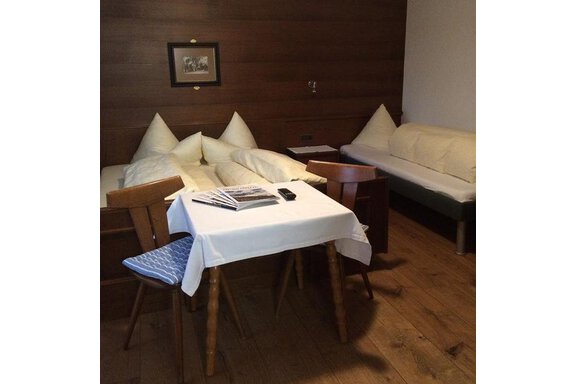 A simple room with bright wooden walls. In the center is a small table with chairs, and there is a bed with pillows. - Gästehaus Martin - Sölden
