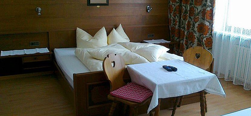 A simple room with wooden walls, a bed, and a table with two chairs. A small remote control lies on the table. - Gästehaus Martin - Sölden