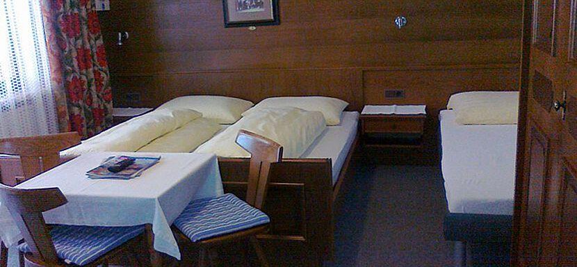 A simple room with two beds and a table. A small picture hangs on the wall, and the windows are decorated with curtains. - Gästehaus Martin - Sölden