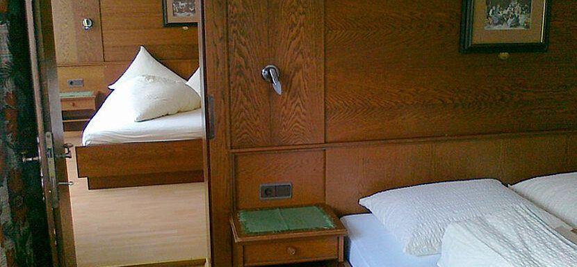 A cozy bedroom with wooden walls and two beds. There are pillows on the beds and small cabinets beside them. - Gästehaus Martin - Sölden