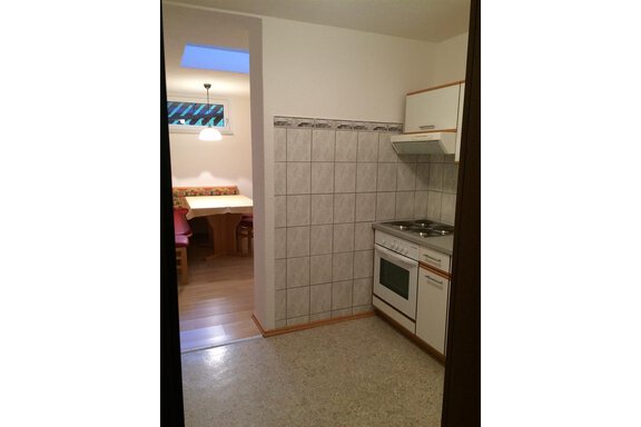 A small kitchen with modern appliances and tiled walls. In the background, a dining area with seating is visible. - Gästehaus Martin - Sölden