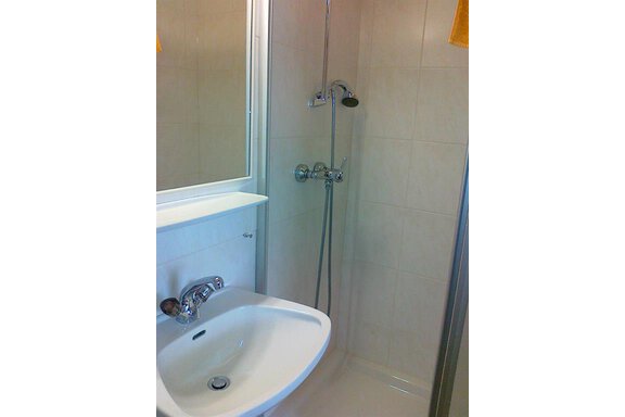 A small bathroom with a shower and sink. The walls are light tiled and there is a mirror above the sink. - Gästehaus Martin - Sölden