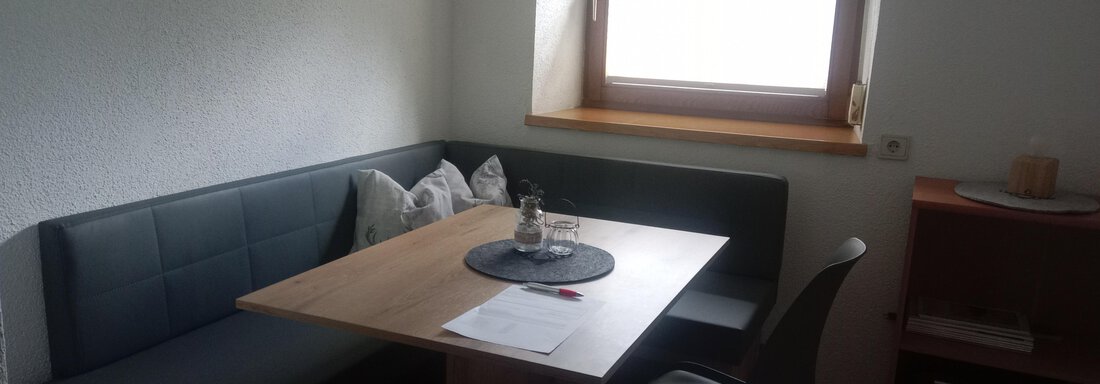 A cozy dining area with a small seating nook and a wooden table. The window provides daylight and a pleasant atmosphere. - Gästehaus Sternberger - Sölden