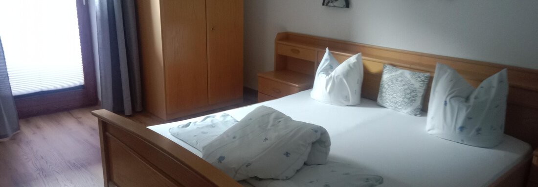 A cozy bedroom with a wooden bed and fresh bedding. The room has access to a balcony and plenty of daylight. - Gästehaus Sternberger - Sölden