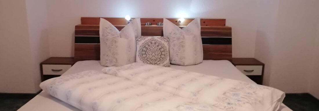 A cozy bedroom with a large bed and pillows. Soft lighting and simple furniture create a relaxed atmosphere. - Gästehaus Sternberger - Sölden